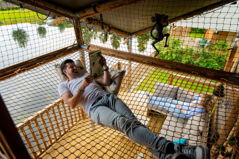 Ein Mann entspannt und liest in einem Hängemattengitter bei Glamping De Rode Vos am See in Noord-Brabant.