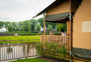 Deux personnes assises sur la terrasse de Glamping De Rode Vos près d’un lac en Brabant-Septentrional, Pays-Bas.