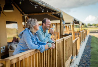 Et par nyder morgenkaffe på terrassen foran glampingtelt ved Glamping De Rode Vos i Noord-Brabant.
