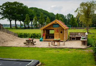 Speelhoek bij Glamping De Rode Vos in Noord-Brabant met houten hut, zand en grasveld.