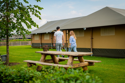 Couple au Glamping De Rode Vos près des tentes et d’une table en bois, cadre vert à Noord-Brabant.