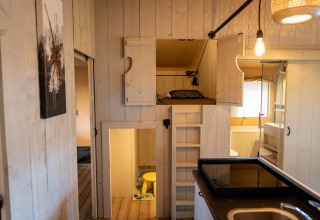Vue intérieure de la tente Glamping De Rode Vos avec lit mezzanine, kitchenette et salle de bain privée.