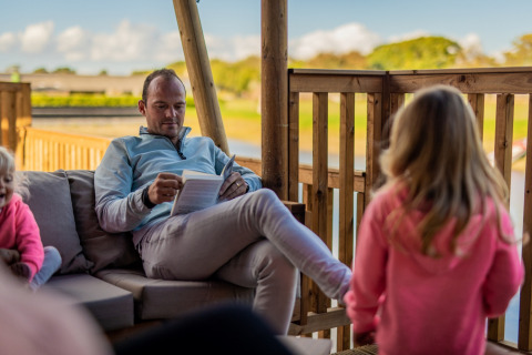 Homme lisant un livre sur la terrasse d’une tente glamping à Glamping De Rode Vos, Noord-Brabant avec enfants.