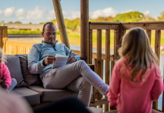Homme lisant un livre sur la terrasse d’une tente glamping à Glamping De Rode Vos, Noord-Brabant avec enfants.
