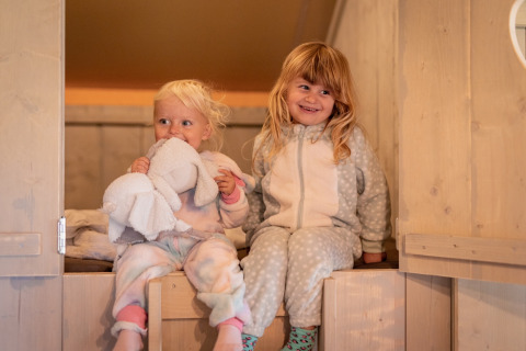 To små børn i pyjamas hygger sig indendørs i et hyggeligt glamping-telt ved Glamping De Rode Vos.
