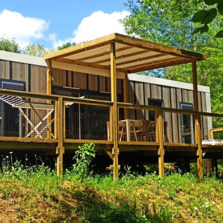 Alloggio glamping Camping Les Charmes - Cottages Dordogne con terrazza in legno immersa nel verde.