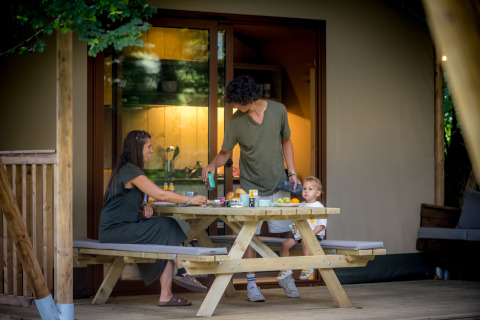 Familie genießt gemeinsames Essen auf der Holzterrasse vor einem Glampingzelt in Urban Gardens Ieper.