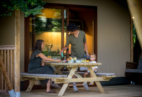 Family enjoys outdoor meal on wooden deck at a glamping tent accommodation in Urban Gardens Ieper, West-Flanders.