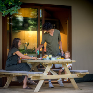 Gezin aan het eten op het houten terras bij een glampingtent in Urban Gardens Ieper, West-Vlaanderen.