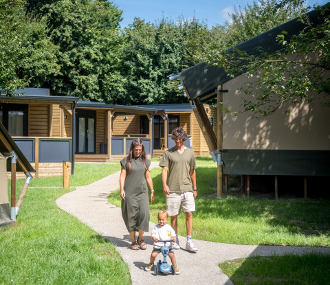 Familia paseando por un sendero en Urban Gardens Ieper - Glampingtenten West-Vlaanderen, rodeados de cabañas glamping.