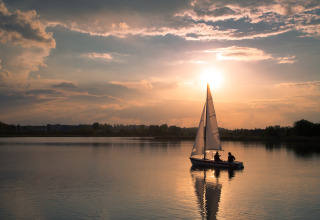 Een rustige zonsondergang met een zeilboot op een meer, ideaal voor een ontspannen vakantie in een glampingpark.