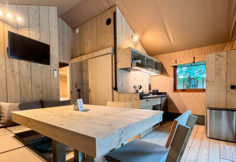 Alojamiento glamping moderno con interior de madera, mesa de comedor, cocina, TV y ventana en Urban Gardens Ieper.