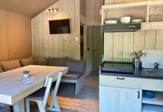 Licht glampinginterieur met houten meubels, kitchenette, bank, tv en eettafel bij Urban Gardens Ieper.