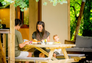 Familie nyder morgenmad udendørs foran en glampingtelt på Urban Gardens Ieper i West-Vlaanderen.