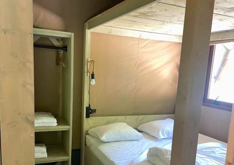 Interieur van een glampingtent met tweepersoonsbed, linnengoed, handdoeken en raam in Urban Gardens Ieper.