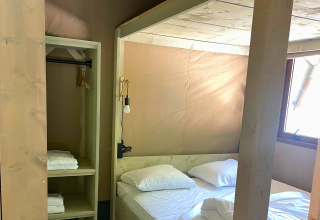 Intérieur d’une tente glamping avec lit double, draps, serviettes et fenêtre à Urban Gardens Ieper.