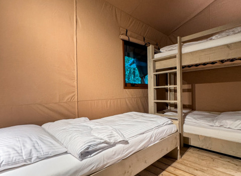 Interior de una tienda glamping en Urban Gardens Ieper, Flandes Occidental, con literas y ventana.