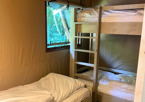 Intérieur d’une tente glamping Urban Gardens Ieper, avec lits superposés et lit simple près d’une fenêtre.