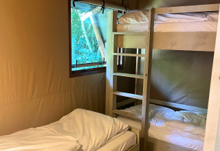 Binnenaanzicht van Urban Gardens Ieper glampingtent met stapelbedden en eenpersoonsbed bij het raam.