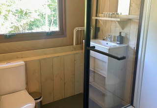 Badeværelse med træpaneler, vindue, toilet, vask og bruser i Urban Gardens Ieper glampingtelte.