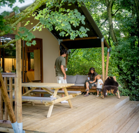 Glamping-Unterkunft bei Urban Gardens Ieper, Westflandern, Familie entspannt auf Holzterrasse.