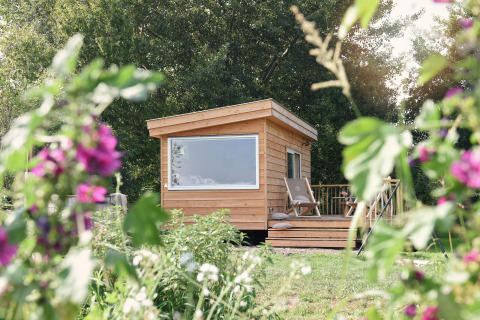 Træhytte til glamping hos Smûk Recreatie - Tiny houses Friesland med blomster i forgrunden.