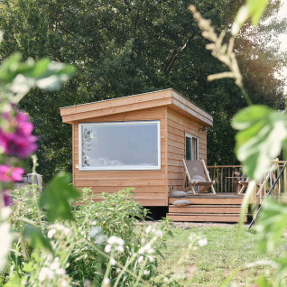 Træhytte til glamping hos Smûk Recreatie - Tiny houses Friesland med blomster i forgrunden.