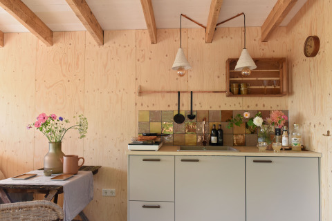 Acogedora cocina pequeña de madera con flores, azulejos retro y vigas vistas en Smûk Recreatie, Tiny houses Friesland.
