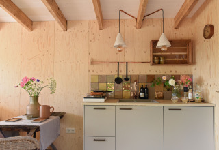 Petite cuisine en bois chaleureuse avec fleurs, carreaux rétro et poutres apparentes chez Smûk Recreatie, Friesland.