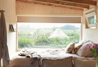 Intérieur douillet de tiny house avec vue sur une tente et nature verdoyante chez Smûk Recreatie, Friesland.