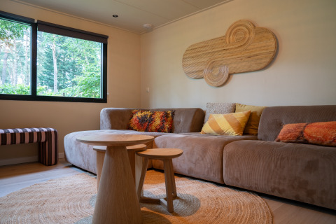 Gezellige glampingaccommodatie bij Camping Twente - Chalet Overijssel met bank, kussens en houten tafels.