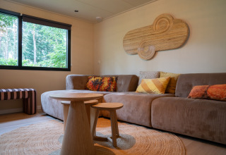 Hébergement glamping confortable au Camping Twente - Chalet Overijssel avec sofa, coussins et tables en bois.