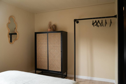 Dormitorio de glamping en Camping Twente - Chalet Overijssel con armario, espejo decorativo y perchero abierto.