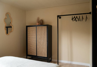 Chambre dans un chalet glamping à Camping Twente Overijssel, avec armoire, miroir et portemanteau ouvert.