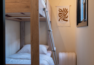 Acogedora habitación con litera, escalera, arte en la pared y ventana en Camping Twente - Chalet Overijssel.