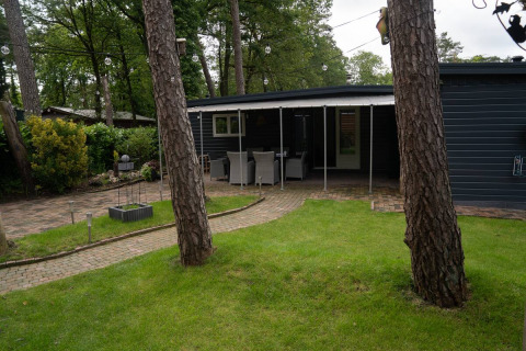 Glamping-Unterkunft Camping Twente - Chalet Overijssel mit Garten, Bäumen und überdachter Terrasse.