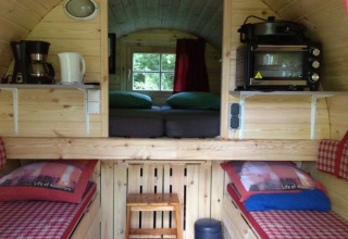 Indvendigt billede af en glampingindkvartering med træpaneler, senge og et lille køkkenområde i Zeeland.