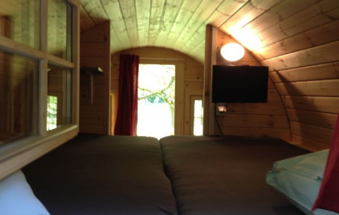 Interior view of glamping accommodation with wooden walls, double bed, window, TV, and light in Zeeland.