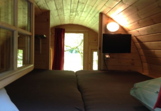 Vista interna di un alloggio glamping con pareti in legno, letto matrimoniale, finestra, TV e luce a Zeeland.