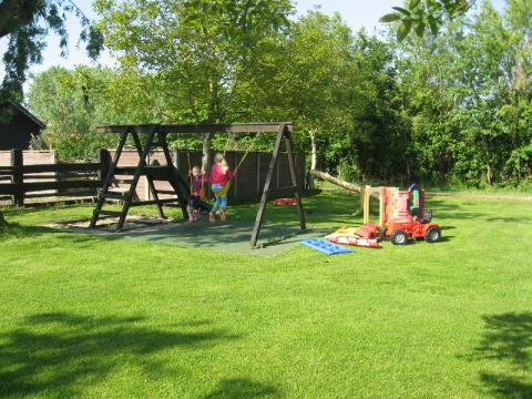 Børnevenlig legeplads med gynger og legetøj på Minicamping De Bokkepsprong i Zeeland på en solrig dag.