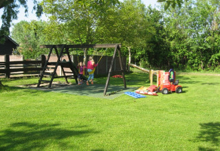 Kinderen spelen op schommels en speelgoed buiten bij Minicamping De Bokkepsprong in Zeeland.