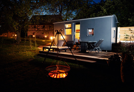 Escena nocturna de glamping en Handwerkerhof Fränkische Schweiz Zigeunerwagen con fogata y terraza.