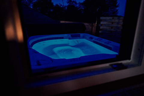Jacuzzi exterior con iluminación azul visto a través de una ventana por la noche en Handwerkerhof Fränkische Schweiz.