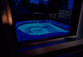 Bubbelbad met blauwe verlichting buiten, ’s avonds gezien door een raam bij Handwerkerhof Fränkische Schweiz.