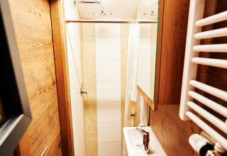 Smalt badeværelse med træpaneler, bruser, toilet og lille håndvask i Handwerkerhof Fränkische Schweiz Zigeunerwagen glamping.