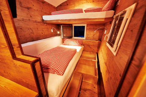 Gezellig interieur van een glampingwagen met houten panelen, stapelbedden en rood geruit beddengoed.