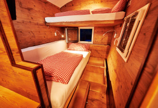 Knusse glampingaccommodatie van binnen met houten wanden, stapelbedden en rood geruit beddengoed.