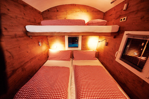 Intérieur d'un hébergement de glamping chaleureux avec lits superposés, parure rouge à carreaux et murs boisés.