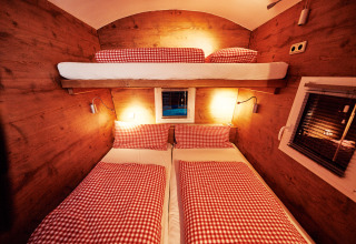 Interieur van een gezellige glampingverblijf met stapelbedden, rood geruit beddengoed en houten wanden.