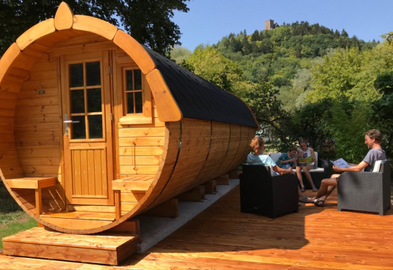 Glamping wine barrel cabin at Camping Alf, Rhineland-Palatinate, people relaxing on a wooden deck.